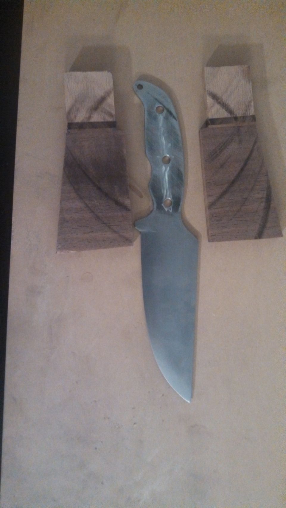 Knife blade with two wooden handle scales on a light brown surface
