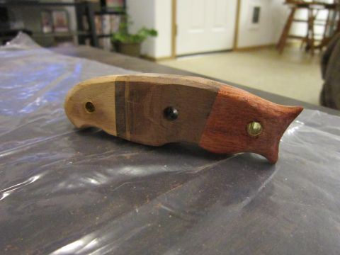 1974 Ford Ranchero - A wooden handle for a knife is shown, constructed from several pieces of wood with brass and black fasteners. The handle is lying on a dark…