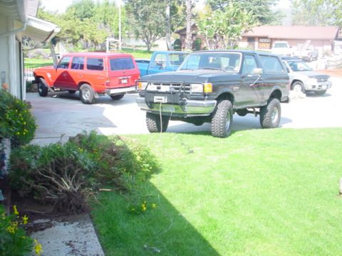 1988 Ford Bronco - A black Ford Bronco is parked on the lawn next to a red SUV and a blue pickup truck.