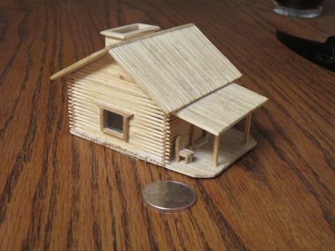 1974 Ford Ranchero - A miniature house made of toothpicks sits on a wooden table next to a coin. The house has a porch with a small chair and a chimney.