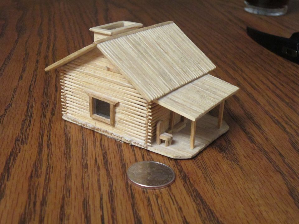 Miniature toothpick house with a porch and chimney on a wooden table.