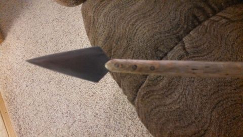 1974 Ford Ranchero - A close-up view of a dark, triangular arrowhead attached to a wooden handle with visible rivets, resting on a textured brown fabric surface.