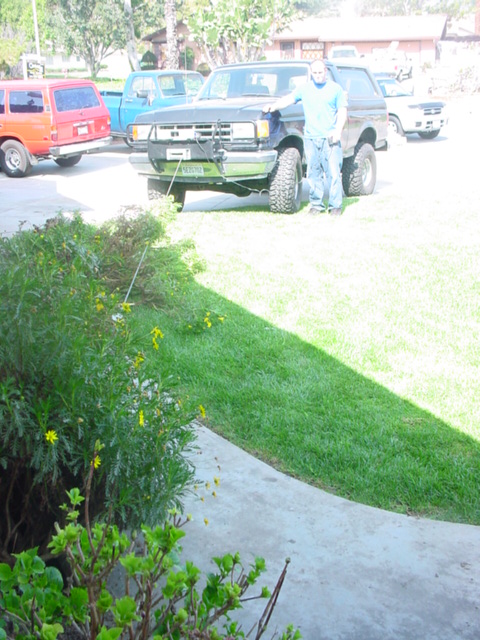 1988 Ford Bronco - A man stands next to a dark blue Ford Bronco, which appears to be a later model than the registry suggests, with other vehicles visible in…