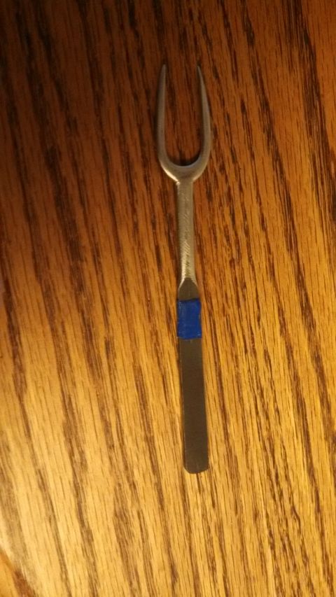 1974 Ford Ranchero - A close-up shot of a small, silver, two-pronged fork with a blue band around its handle rests on a wooden surface.