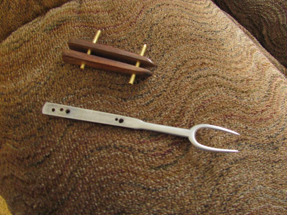 Wooden object with brass pins and a metal carving fork on a brown textured surface.