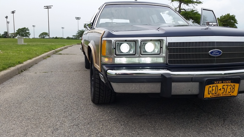 Dark blue Ford wagon with woodgrain trim, headlights on, low front angle, NY plate GED-5738