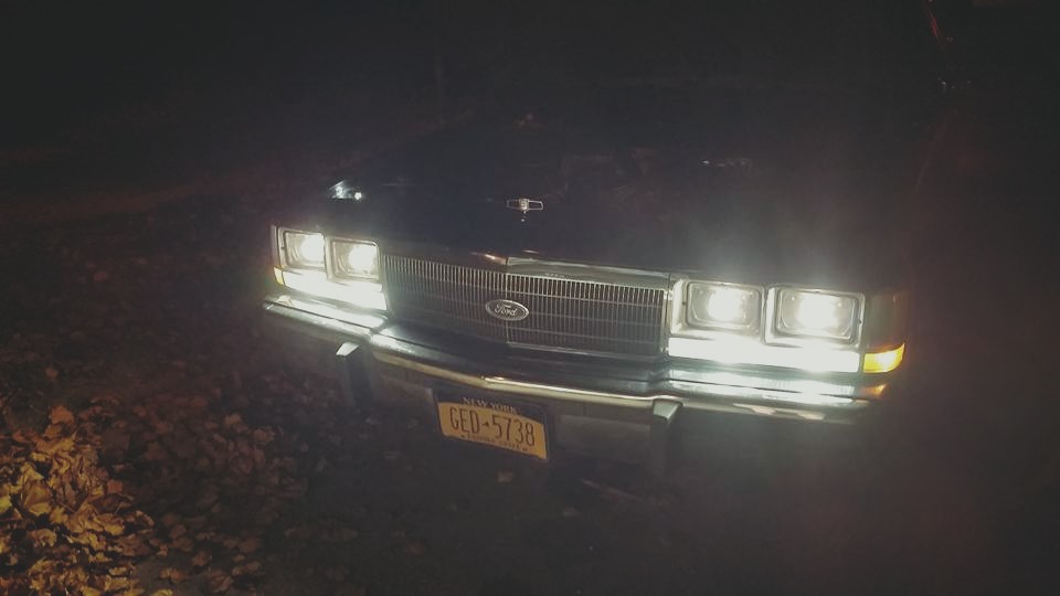 Front of dark Ford with quad headlights on at night, NY plate GED-5738, leaves on ground