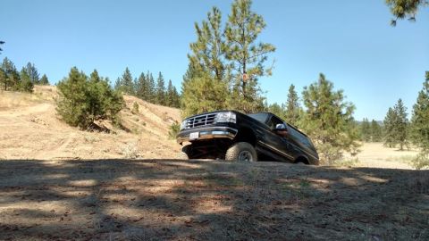 1995 Ford Bronco - An off-road vehicle navigates a dusty trail under a clear blue sky.