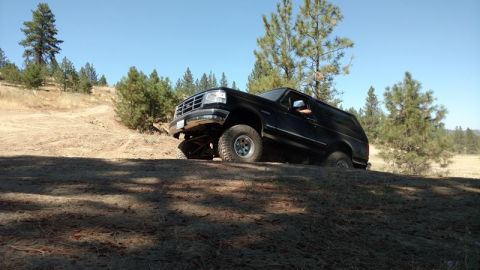 1995 Ford Bronco - A black SUV navigates a dirt incline under a clear blue sky.