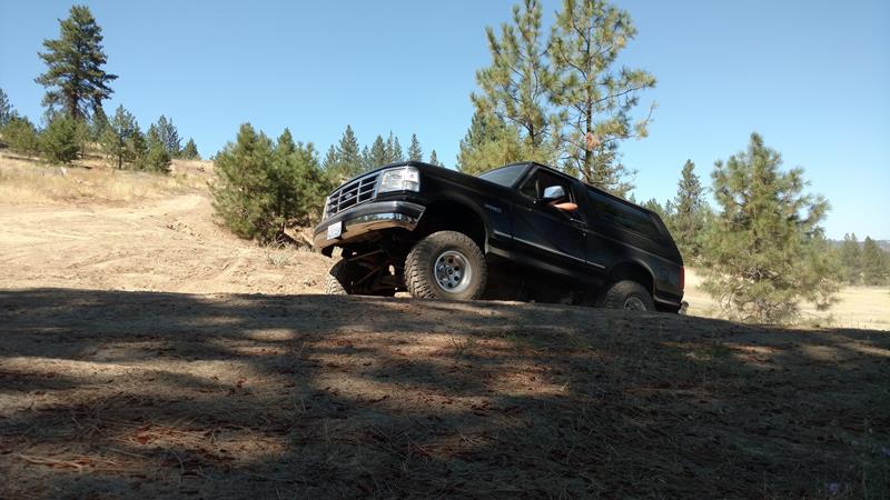 Black SUV on a dirt hill, front-left tire angled up