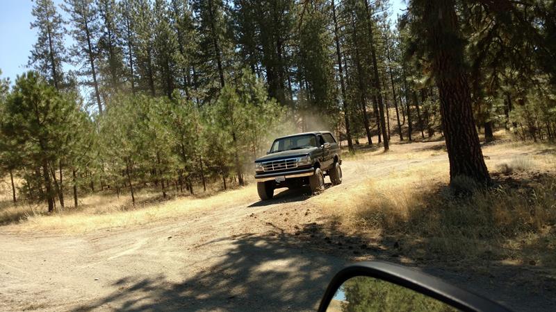 Dark 1992 Ford Bronco driving on a dirt road in a forest