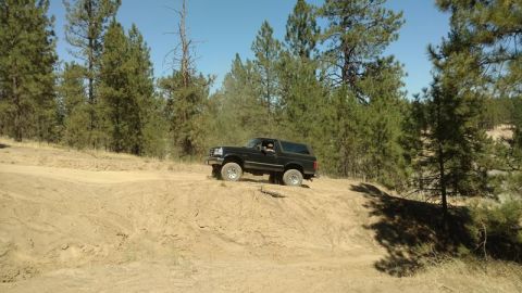 1995 Ford Bronco - Black 1995 Ford Bronco navigates a sandy incline in a wooded area.