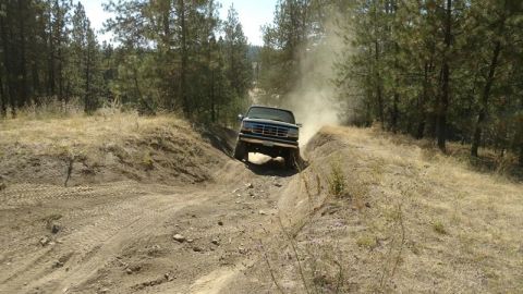 1995 Ford Bronco - A 1995 Ford Bronco navigates a dusty off-road trail, kicking up a cloud of dirt.