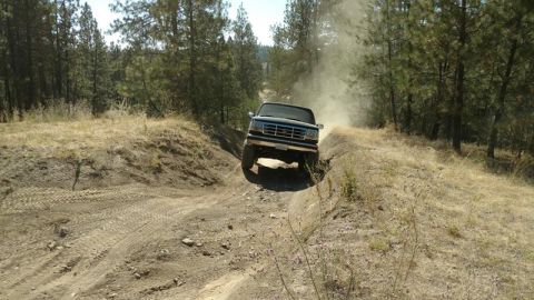 1995 Ford Bronco - Ford Bronco navigates a dirt trail, kicking up dust.