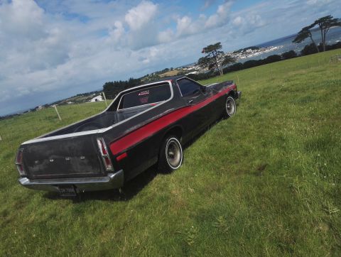 1974 Ford Ranchero - A black 1974 Ford Ranchero with a red stripe sits on a grassy hill overlooking a coastal town.