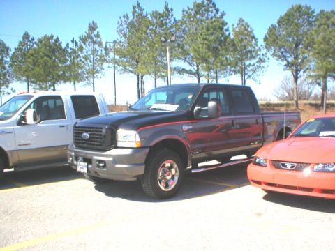 1989 Ford Crown Victoria - A black Ford F-250 Super Duty pickup truck is parked next to a white truck and an orange Ford Mustang.