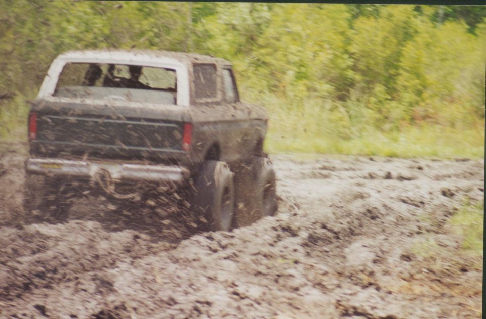 Lifted Ford Bronco running through a mud pit, mud flying from rear tires