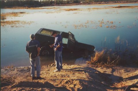 1993 Ford Bronco - A black 1993 Ford Bronco is partially submerged in water as two men observe the scene.
