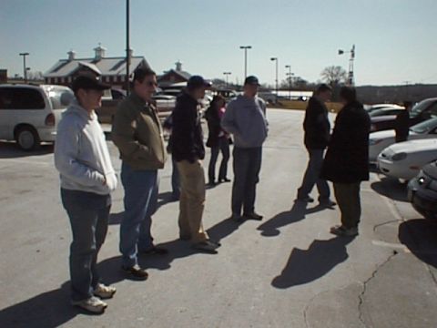 1999 Ford Taurus - A group of people stand in a parking lot on a sunny day, with a white van and other vehicles in the background.