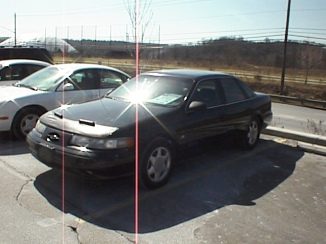 Dark 1999 Ford Taurus sedan parked, 3q-front view, with hood cover