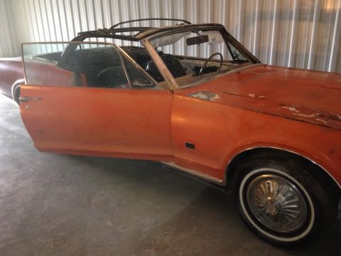 1968 Mercury Cougar - An orange 1968 Mercury Cougar convertible sits in a garage with its door ajar, revealing a second vehicle in the background.