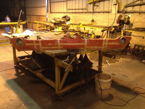 1968 Mercury Cougar - A red car bumper is clamped in a vise on a workbench in a cluttered workshop.