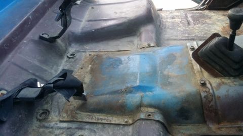 1978 Chevrolet C/K Pickup - The interior floor of a truck shows signs of rust and wear, with seatbelt anchors and a shifter boot visible.