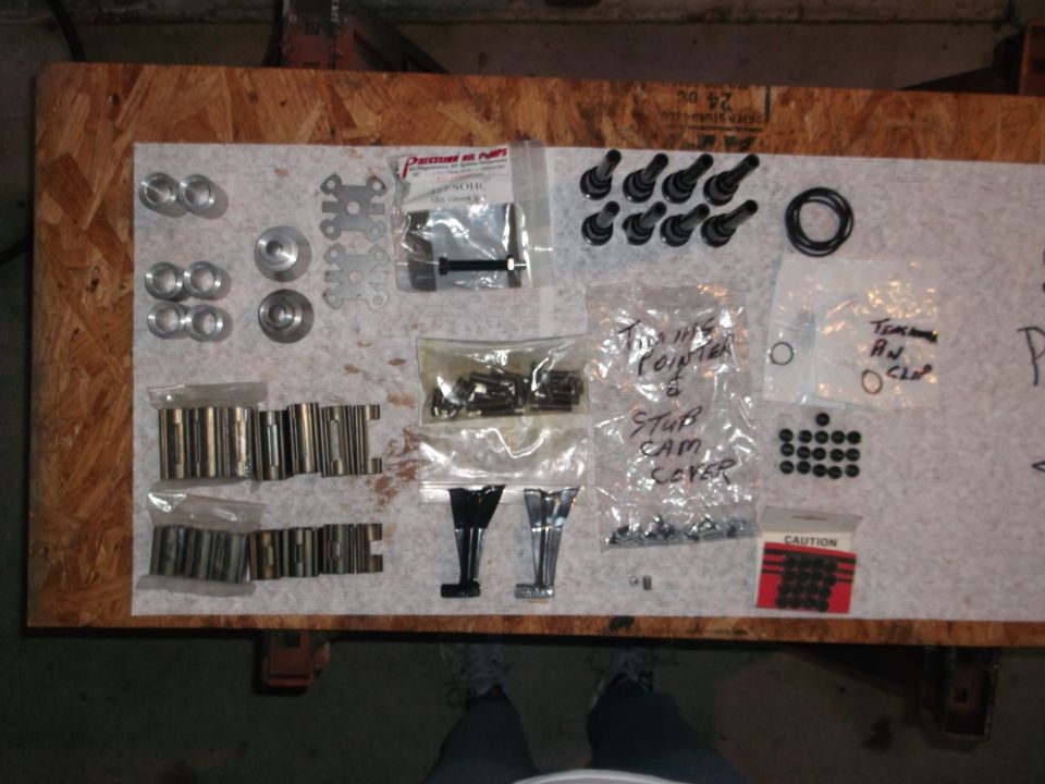 Engine parts including lifters, valves, and seals arranged on a wooden surface