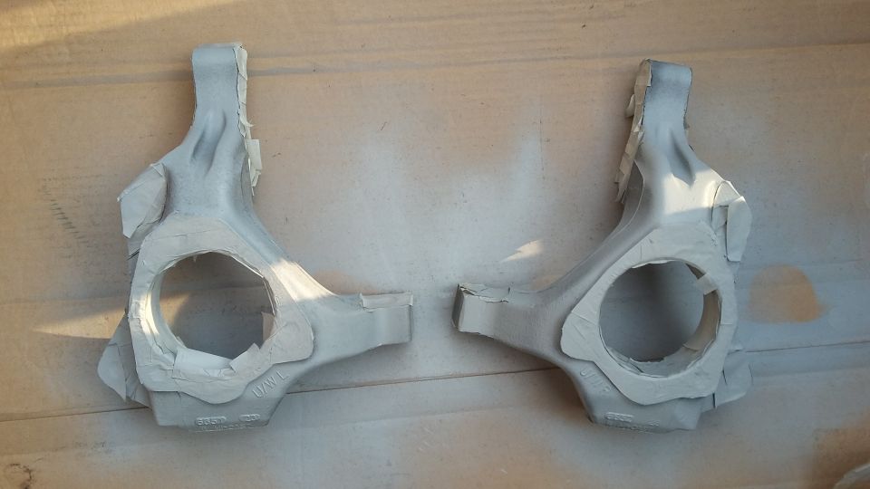 Pair of gray suspension knuckles with masking tape, on a wooden surface