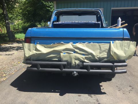 1979 Ford Bronco - Rear view of a blue pickup truck, partially covered with masking tape and paper, with a black brush guard installed over the bumper.
