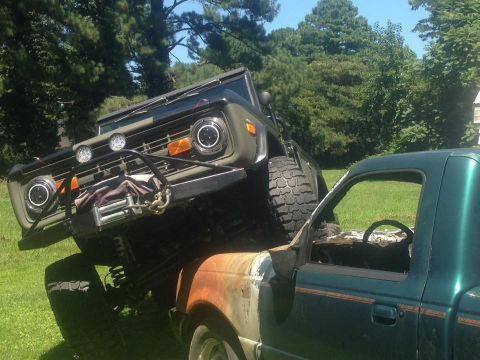 1972 Ford Bronco - A 1972 Ford Bronco is precariously perched on top of a green pickup truck.