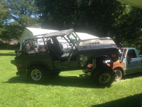1972 Ford Bronco - A modified SUV with a roll cage and soft top is parked on a grassy lawn next to a pickup truck.