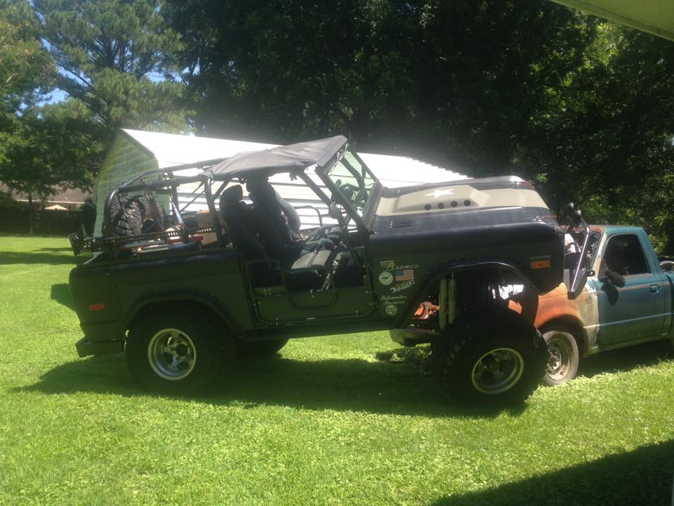 Off-road SUV with roll cage and soft top parked on grass next to a pickup truck