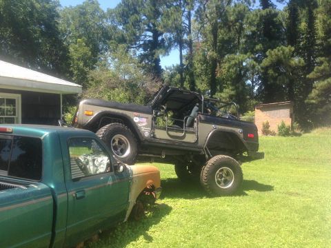 1972 Ford Bronco - A lifted Ford Bronco sits in a grassy yard next to a green pickup truck.