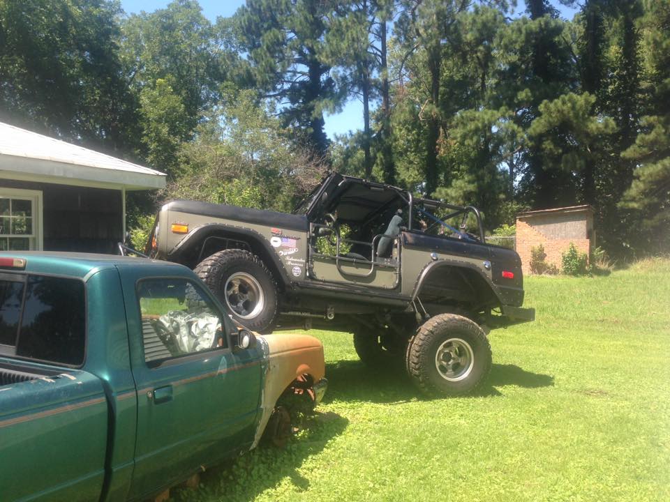 Gray Ford Bronco with black top, lifted, doors removed, parked next to a green pickup truck