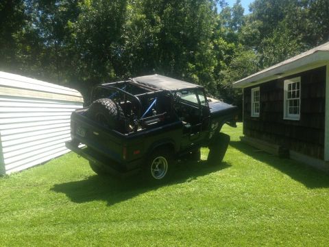 1972 Ford Bronco - A black 1972 Ford Bronco, equipped with a roll cage and spare tire, sits in a grassy yard next to a building.