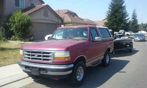 1995 Ford Bronco - A red 1995 Ford Bronco is parked on a residential street, hitched to a boat trailer.
