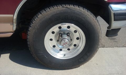 1995 Ford Bronco - A close-up view of a SALOM tire mounted on a silver alloy wheel, attached to a maroon vehicle.