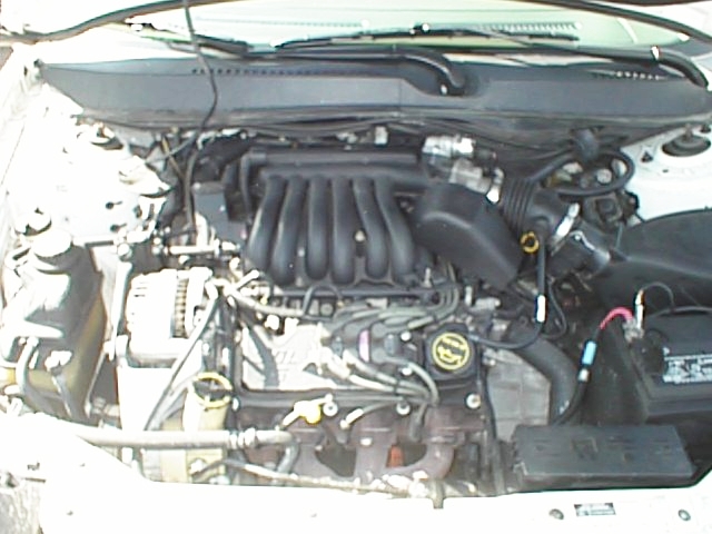 Engine bay view of a 1999 Ford Taurus showing the V6 engine and battery