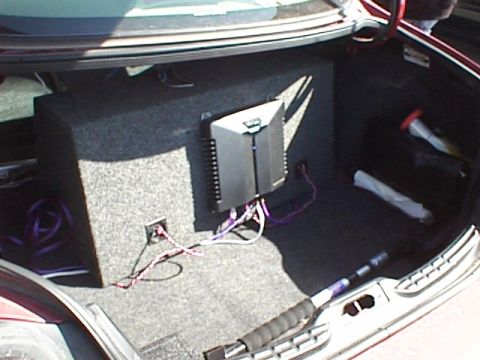 1999 Ford Taurus - The trunk of a vehicle contains a subwoofer box and an amplifier, with wiring visible.