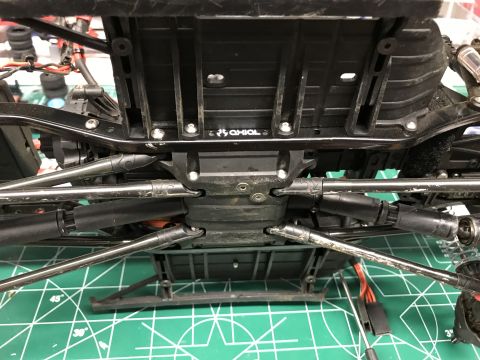 1989 Ford Bronco - Close-up of an RC car's chassis underside, revealing suspension and drivetrain parts. The Axial logo is visible.