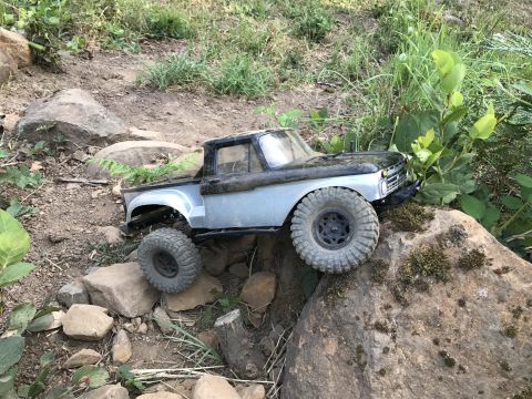 1989 Ford Bronco - A remote-controlled truck navigates a rocky terrain with lush green foliage.