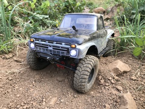 1989 Ford Bronco - This remote-controlled truck is navigating a rough, outdoor terrain with rocks and plants.