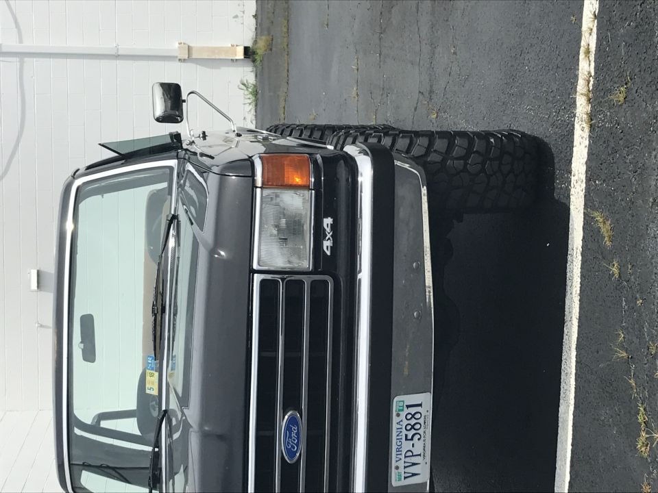 Dark gray Ford Bronco with chrome grille and 4x4 badge. Large off-road tires visible