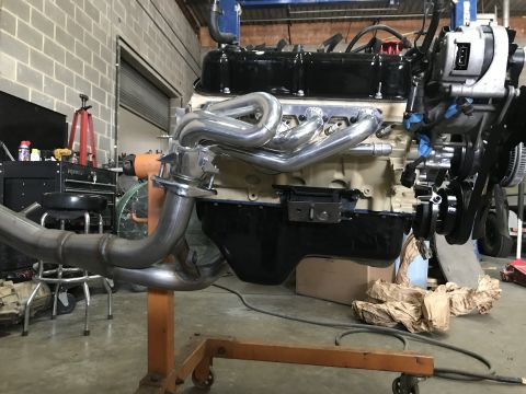 1990 Ford Bronco - Engine assembly with custom exhaust headers and chrome components, mounted on an engine stand in a workshop.