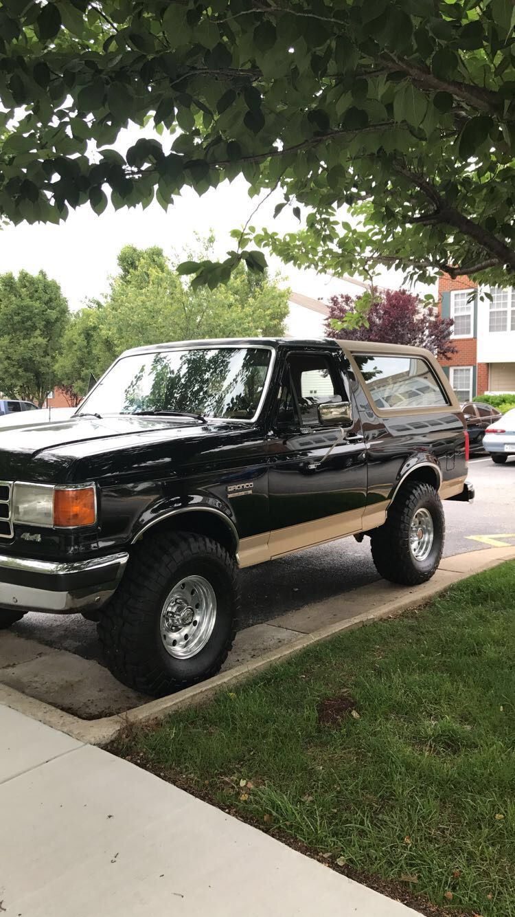 Black and tan Ford Bronco parked on a curb, side view