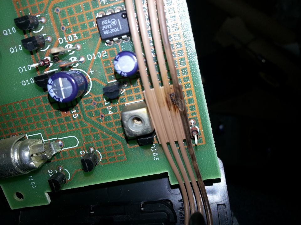 Close-up of a burned electronic circuit board with wires and components. Text '1002780' visible on a chip