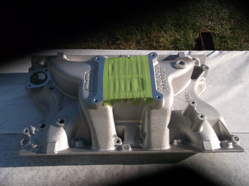 Aluminum intake manifold with green tape covering the carburetor mounting surface. Part number visible