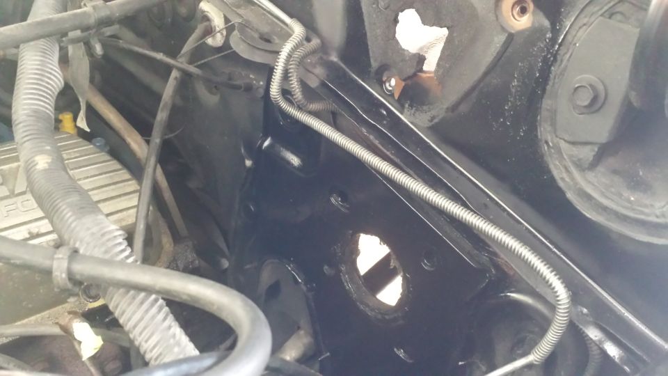 Close-up of engine bay with black painted metal, hoses, and wiring