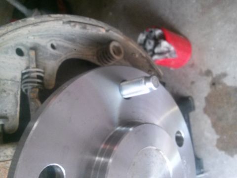 1996 Ford Bronco - Close-up of a car's brake drum and hub assembly, with lug nuts in a red container.